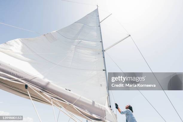 sailboat captain balancing on deck next to mainsail. taking an adventurous boat cruise. - voile bateau photos et images de collection