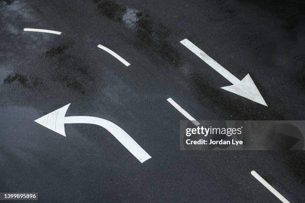 two directional signs with white turn left arrow and right go straight arrow painted on asphalt - dividing line road marking fotografías e imágenes de stock