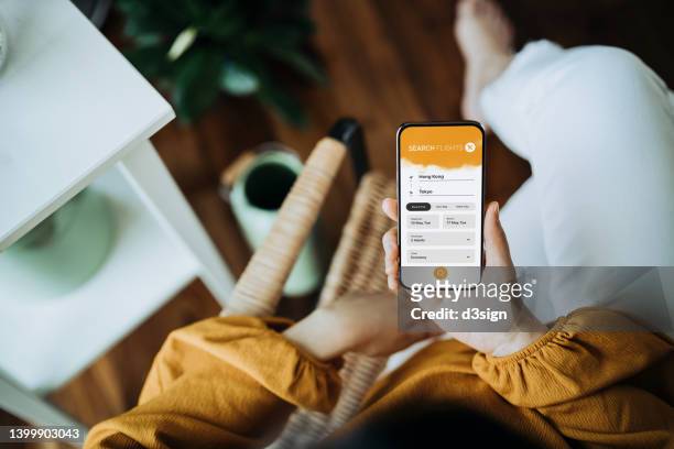 overhead view of young asian woman booking flight tickets on airline website online with smartphone in living room at home. travel planning. booking a holiday online. business person planning business trip - paid search stock pictures, royalty-free photos & images