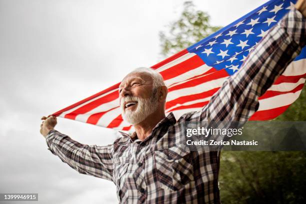 smiling mature american patriot holding the usa flag - veteran stock pictures, royalty-free photos & images