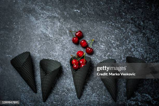 schwarze eistüten und frische kirschen auf schwarzem hintergrund. stockfoto - black cherries stock-fotos und bilder