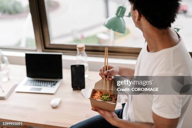 man eating takeout at the office while looking through the sale. - telecommuting eating stock pictures, royalty-free photos & images