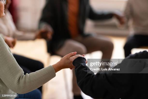 support group holding hands and praying during therapy session - anonyme alkoholiker stock-fotos und bilder