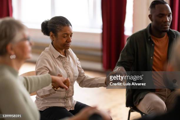 mature woman holding hands with attendees during support group meeting - self harm stock-fotos und bilder