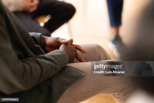 close-up of a man sitting in a circle during group therapy with his hands clasped - rehabilitation meeting stock pictures, royalty-free photos & images