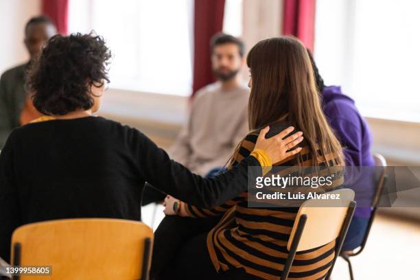 supportive people consoling a sad woman during group therapy session - alcolismo foto e immagini stock