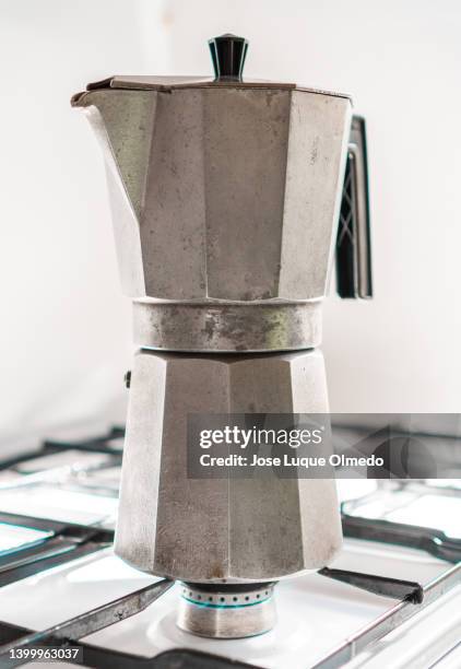 old metal coffee maker placed on burning gas cooker in bright kitchen at home. making coffee in italian moka pot. - moka pot stockfoto's en -beelden