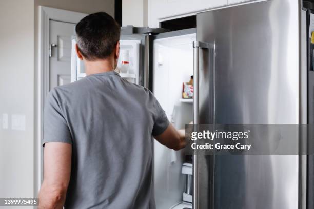 man reaches into refrigerator - refrigerator stock pictures, royalty-free photos & images