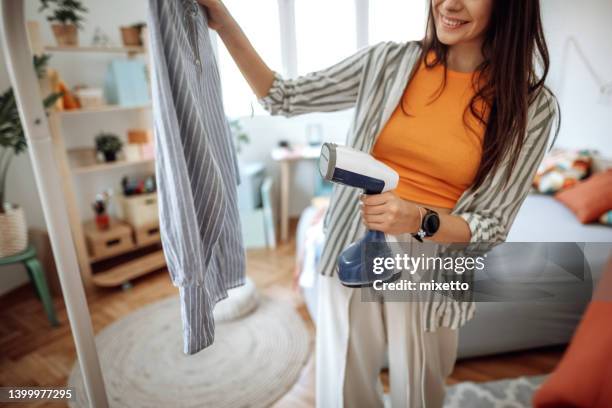 woman is steaming blue stripped shirt in room - metallic dress stock pictures, royalty-free photos & images