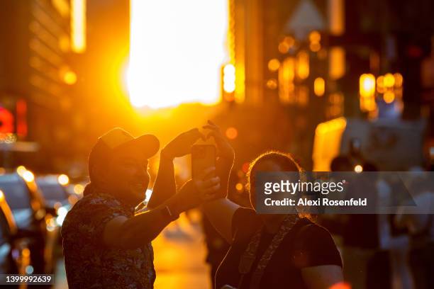 People make a heart with their hands on 42nd Street to watch the sun set during Manhattanhenge in Times Square on May 29, 2022 in New York City....