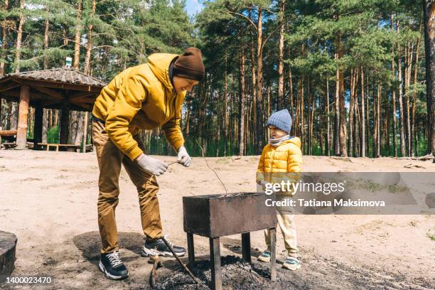 dad and son make a fire in the barbecue in the forest. sunny day, yellow green colors. - fathers day lunch stock pictures, royalty-free photos & images
