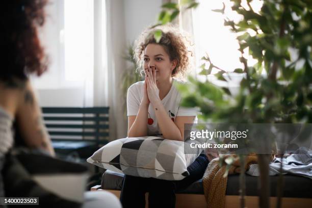 young woman with hands covering mouth with surprise listening to her friend - hand voor de mond stockfoto's en -beelden