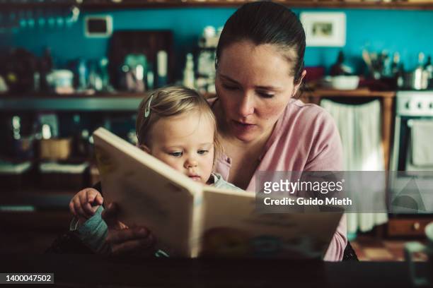mother and her toddler girl looking at picture book together. - story book stock-fotos und bilder
