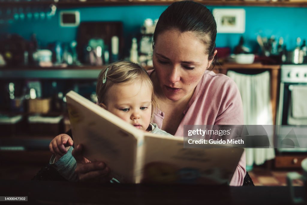 Mother and her toddler girl looking at picture book together.
