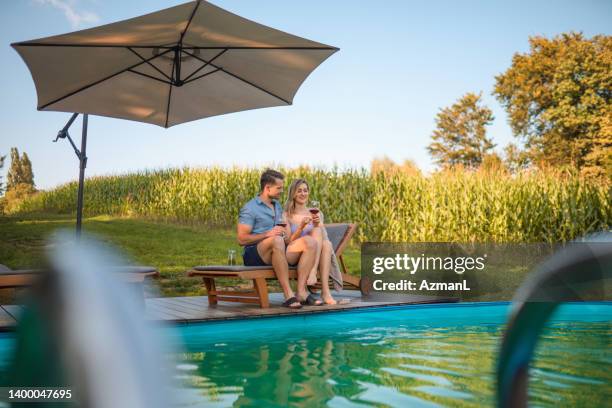 pareja joven relajándose junto a la piscina en glamping resort - sombrilla fotografías e imágenes de stock