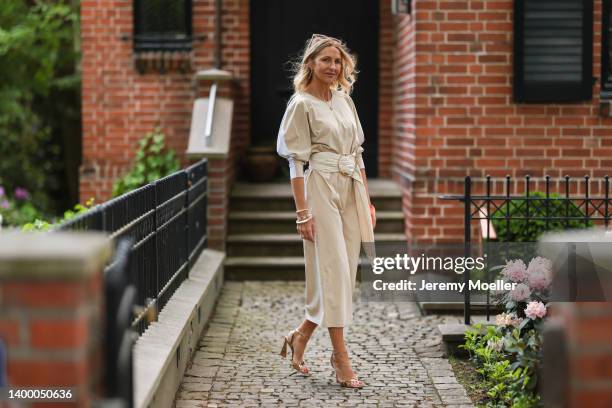 Sue Giers is seen wearing SoSue beige long dress, Sergio Rossi gold heels, Jacquemus gold mini bag earring, Nanushka long beige belt and Celine...