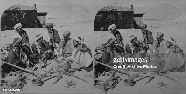 Stereoscopic image showing Bedouins, smoking from long pipes, as they sit at a camp on the Sinai Peninsula, Palestine, circa 1895.