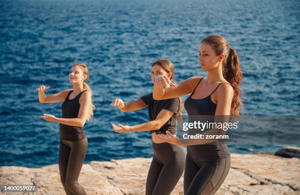 three young women doing tai chi on flat rock by the sea - practising tai-chi stock pictures, royalty-free photos & images