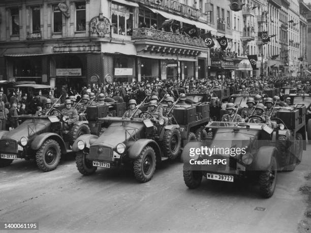 Crowds of people look on as a motorised formation of Military District III Wehrmacht Heer Krupp Protze Kfz 69 six wheeled artillery towing tractors...