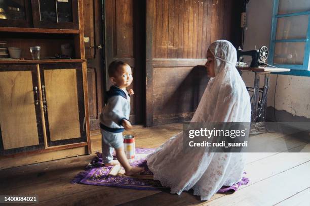 muslim woman praying sholat when her baby playing around - trust god stock pictures, royalty-free photos & images