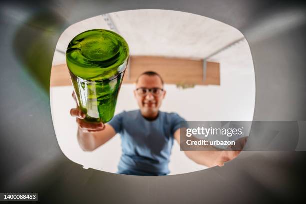 junger mann legt glasflasche in den papierkorb - blick durch kameraobjektiv stock-fotos und bilder