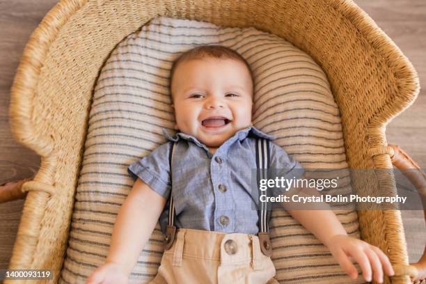a 22-week-old baby boy wearing a blue outfit with suspenders & laying in a cozy cream striped cotton blanket in a seagrass moses basket - tuinbroek stockfoto's en -beelden
