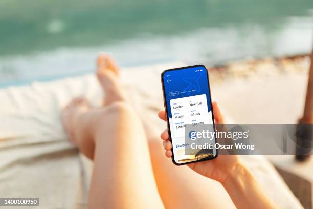 cropped shot of female hand booking a flight via mobile app on smart phone at poolside - booking hotel foto e immagini stock