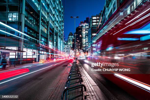 autobus rossi di londra che sfrecciano attraverso la strada notturna dei grattacieli della città - city of london foto e immagini stock