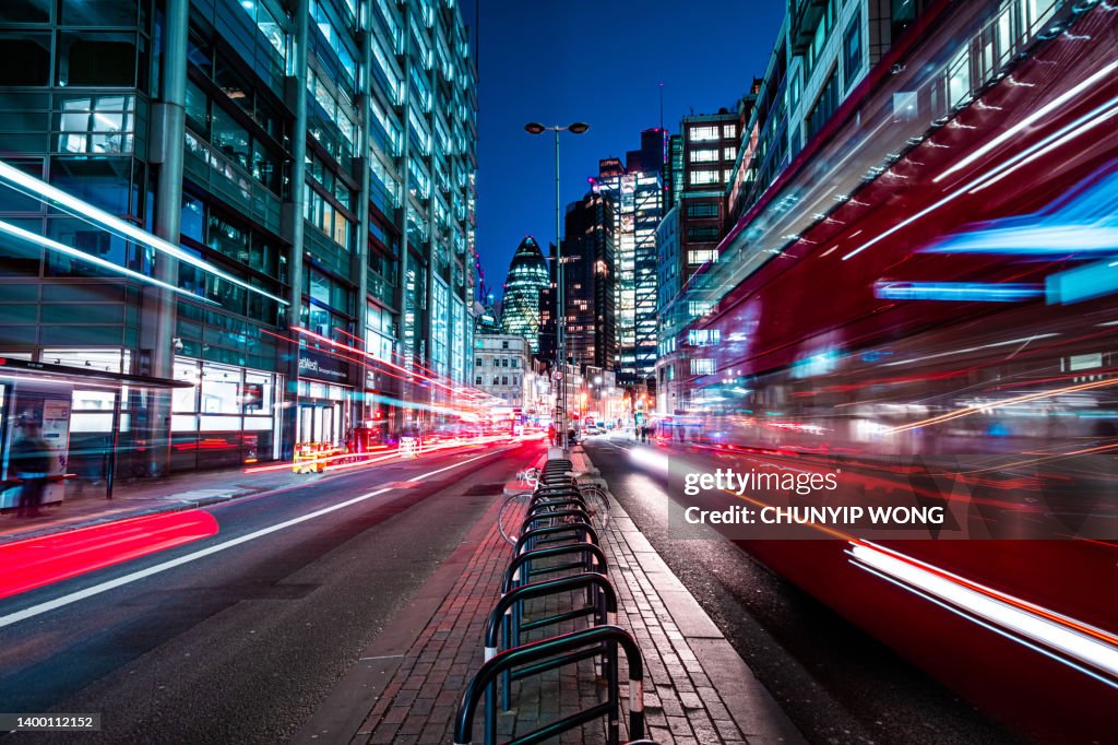 London red buses zooming through City skyscrapers night street