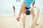 Closeup of unknown athletic squash player using a racket to hit a ball during a court game. Fit active mixed race male athlete training and playing in a sports centre. Healthy cardio and motion blur
