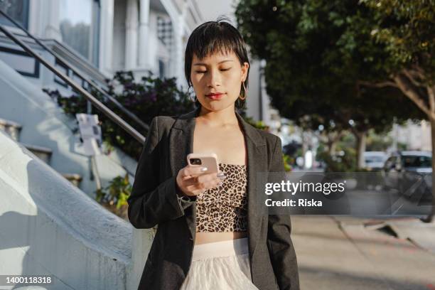 portrait of a young chinese woman in the city, looking at the smart phone - san francisco design center stock pictures, royalty-free photos & images