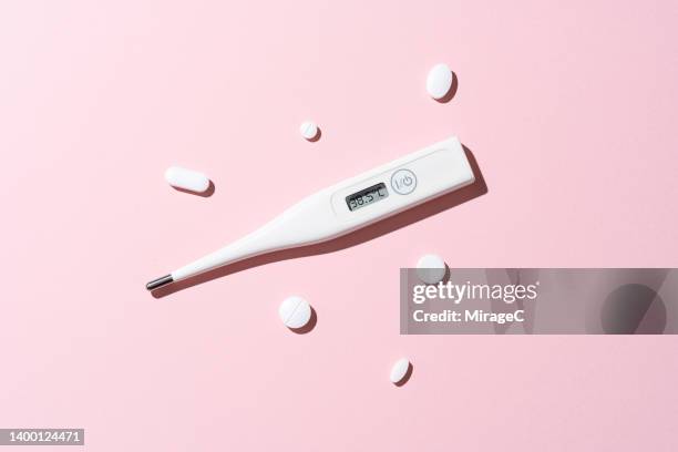 digital thermometer displays 38.5℃ with white pills on pink - pijnstiller stockfoto's en -beelden