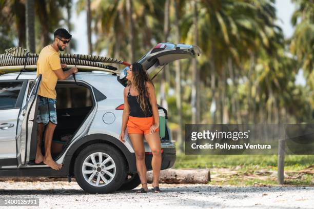 surfers traveling by car - couple on the beach with car stockfoto's en -beelden