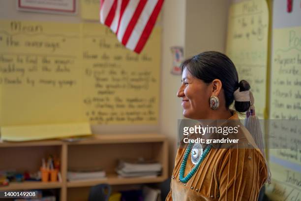 lächelnde junge lehrerin an der vorderseite ihres klassenzimmers, die ihre jungen schüler anspricht und unterrichtet - indianer stock-fotos und bilder