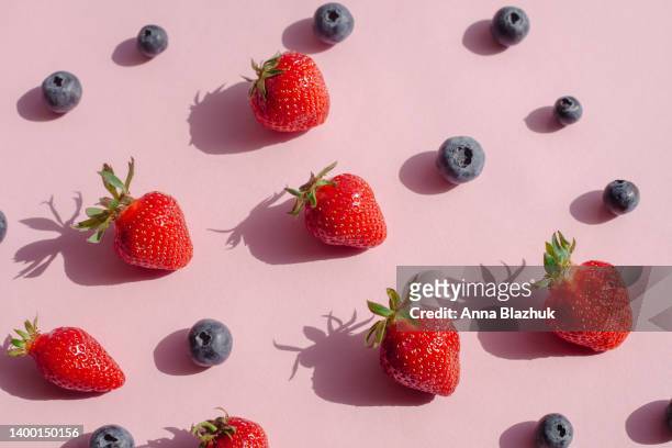 blueberry and strawberry fruits in bright sunlight with shadows over pink background - berry foto e immagini stock