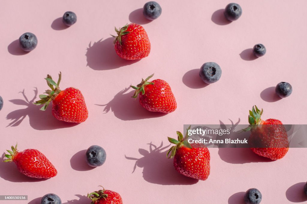 Blueberry and strawberry fruits in bright sunlight with shadows over pink background