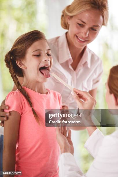 mother and girl during a throat exam by a female doctor - blonde girl sticking out her tongue stock pictures, royalty-free photos & images