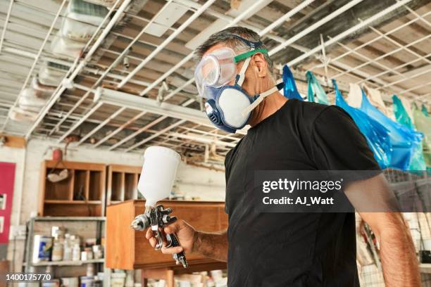 schreiner im atemschutzgerät mit holzfärbespritzpistole in seiner werkstatt - atemschutzmasken stock-fotos und bilder