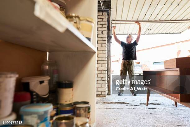 senior carpenter opening his workshop shutter - shop shutter stock pictures, royalty-free photos & images