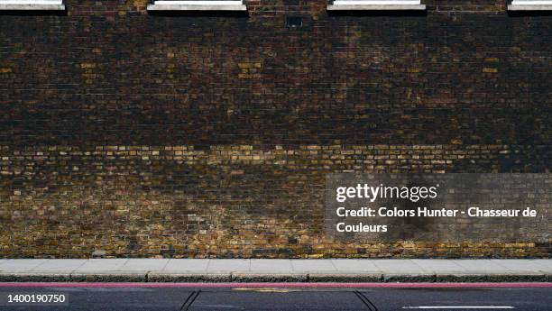 very dirty and weathered dark brick wall with sidewalk and empty street in london - wandmalerei stock-fotos und bilder