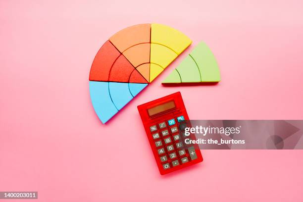 high angle view of a pie chart made of colorful building blocks and red calculator on pink background - education retirement stock-fotos und bilder