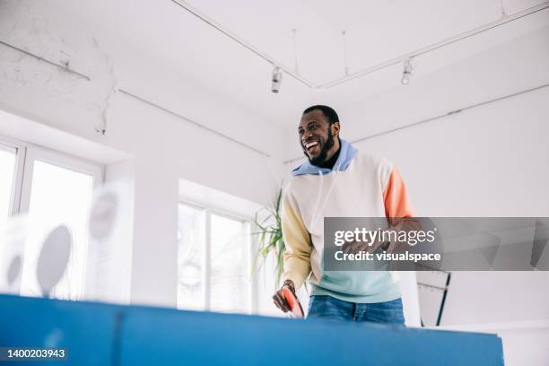 mid adult man playing table tennis at the office - men's table tennis stock pictures, royalty-free photos & images