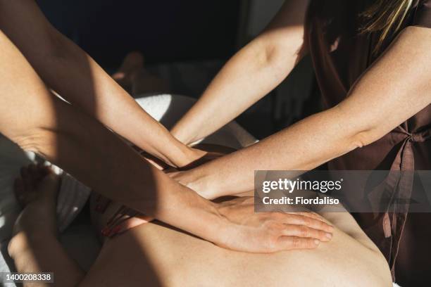 a woman massage therapist in a massage suit uniform teaches massage techniques to a man in a white t-shirt. two hands massage for a woman lying on a massage table in an alternative therapy room - osteopata foto e immagini stock
