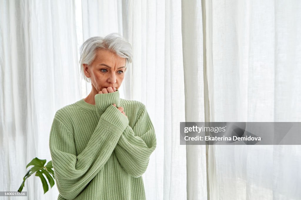 Woman with gray hair nervously bites her nails at the window