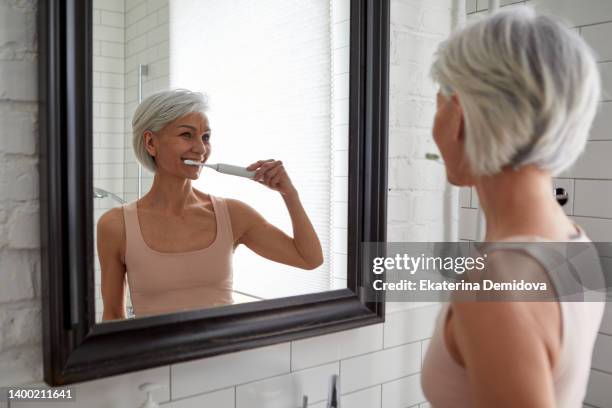 elderly female brushing teeth at home - woman teeth stock-fotos und bilder