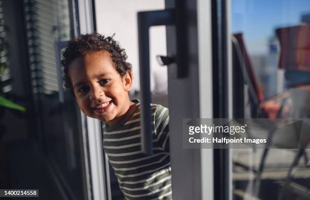 little multiracial boy standing in the balcony door at home. - sliding door stock-fotos und bilder