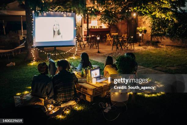 freunde, die auf dem videoprojektor im hinterhofgarten film schauen - open air kino stock-fotos und bilder