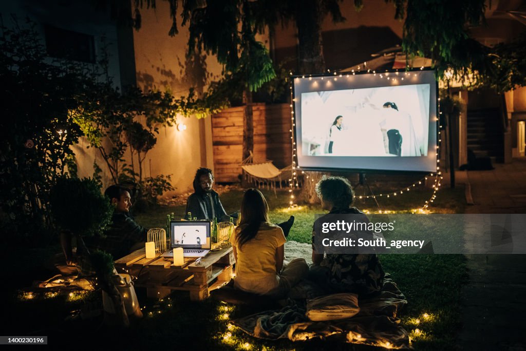 Freunde, die auf dem Videoprojektor im Hinterhofgarten Film schauen