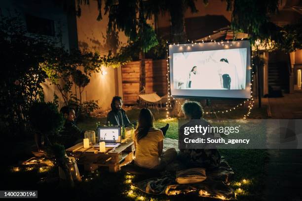 friends watching movie on the video projector in the backyard garden - summer lights stockfoto's en -beelden