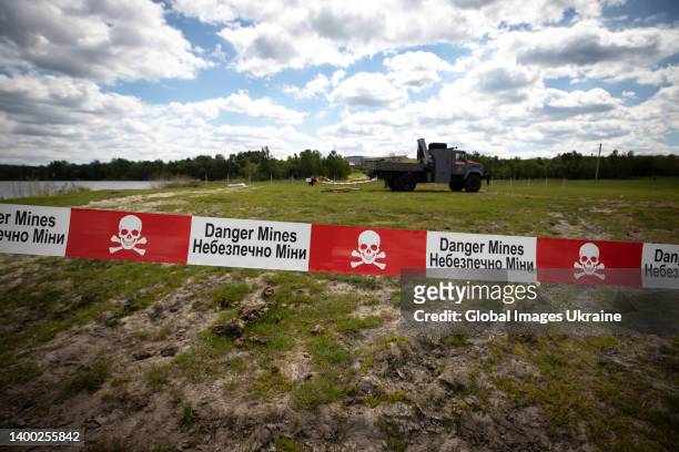 Danger Mine" sign is taped around the area as Ukrainian bomb disposal experts and de-mining teams clear a lake and field of unexploded munitions and...